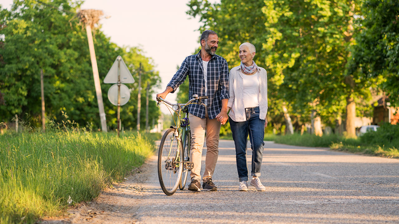 Retiree couple walking on the road while the man holding the bike